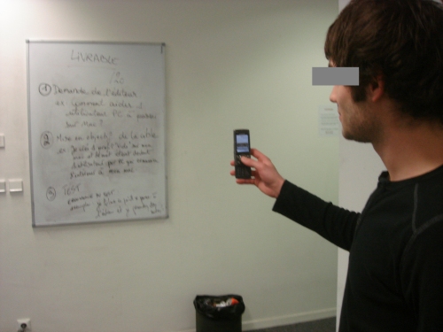 Un élève prend en photo avec son portable un tableau blanc contenant la liste des tâches à faire.